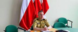 Komendant Główny Państowej Straży Pożarnej nadbryg. Andrzej Bartkowiak w czasie wideokonferencji dotyczącej działań w walce z trzecią falą pandemii COVID-19. W tle flagi narodowe.