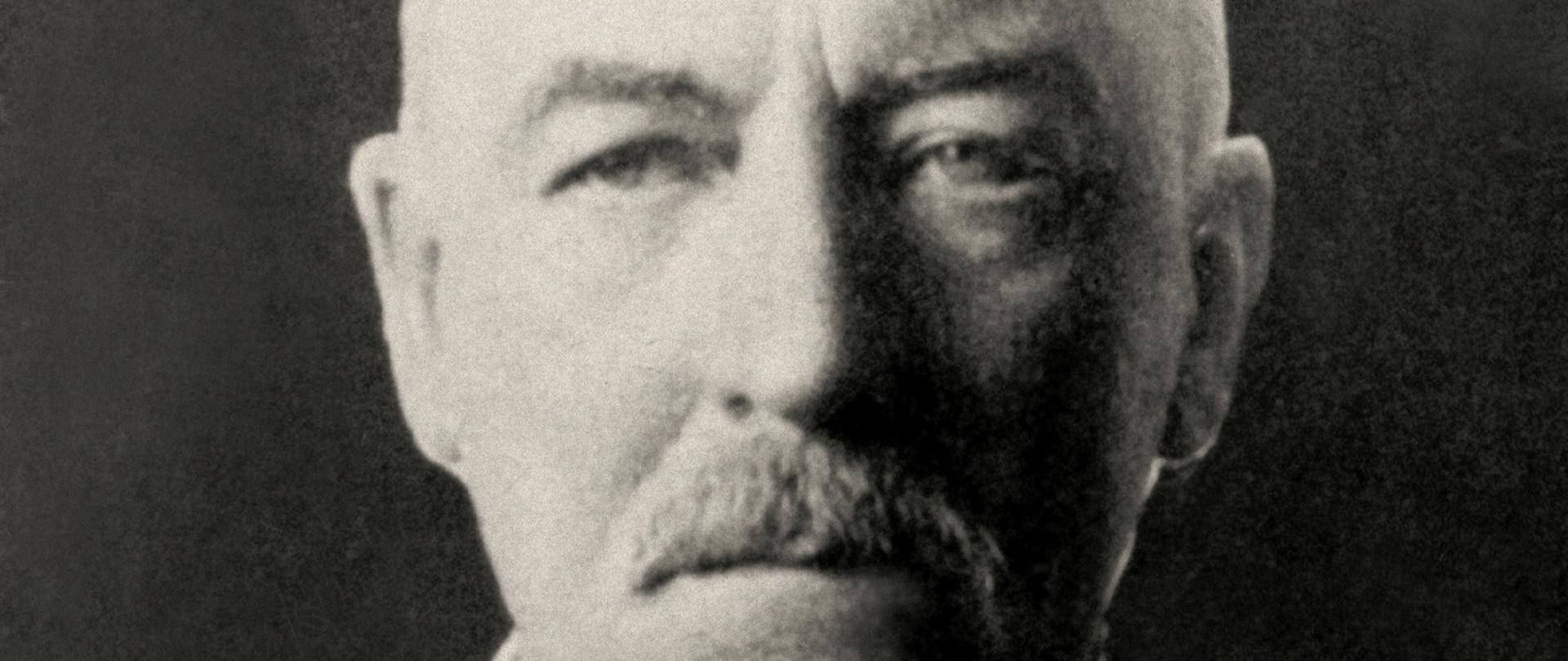 Gabriel Narutowicz - czarno-biały portret starszego łysiejącego mężczyzny, po bokach nieco siwych włosów, wąsy, ciemna marynarka, mucha w paski.