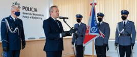 Przemawia wojewoda Mikołaj Bogdanowicz, na drugim planie sztandar Komendy Wojewódzkiej Policji oraz Komendant Wojewódzki insp. Piotr Leciejewski