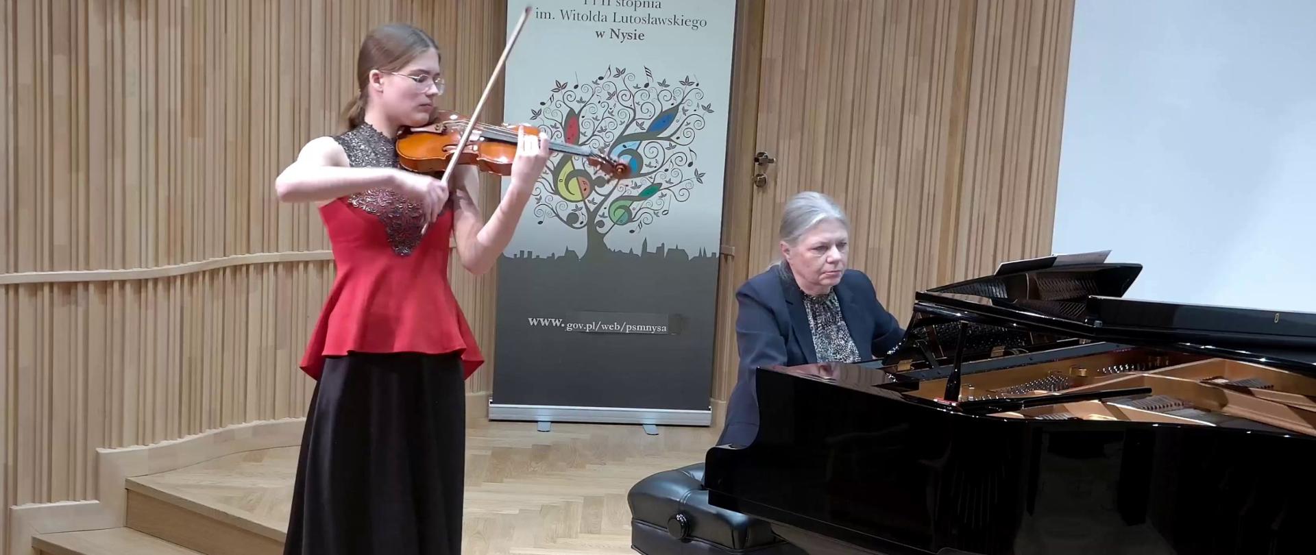Zdjęcie. Na estradzie grają: z lewej strony skrzypaczka, z prawej na dużym czarnym fortepianie pianistka. w tle stoi baner PSM Nysa.