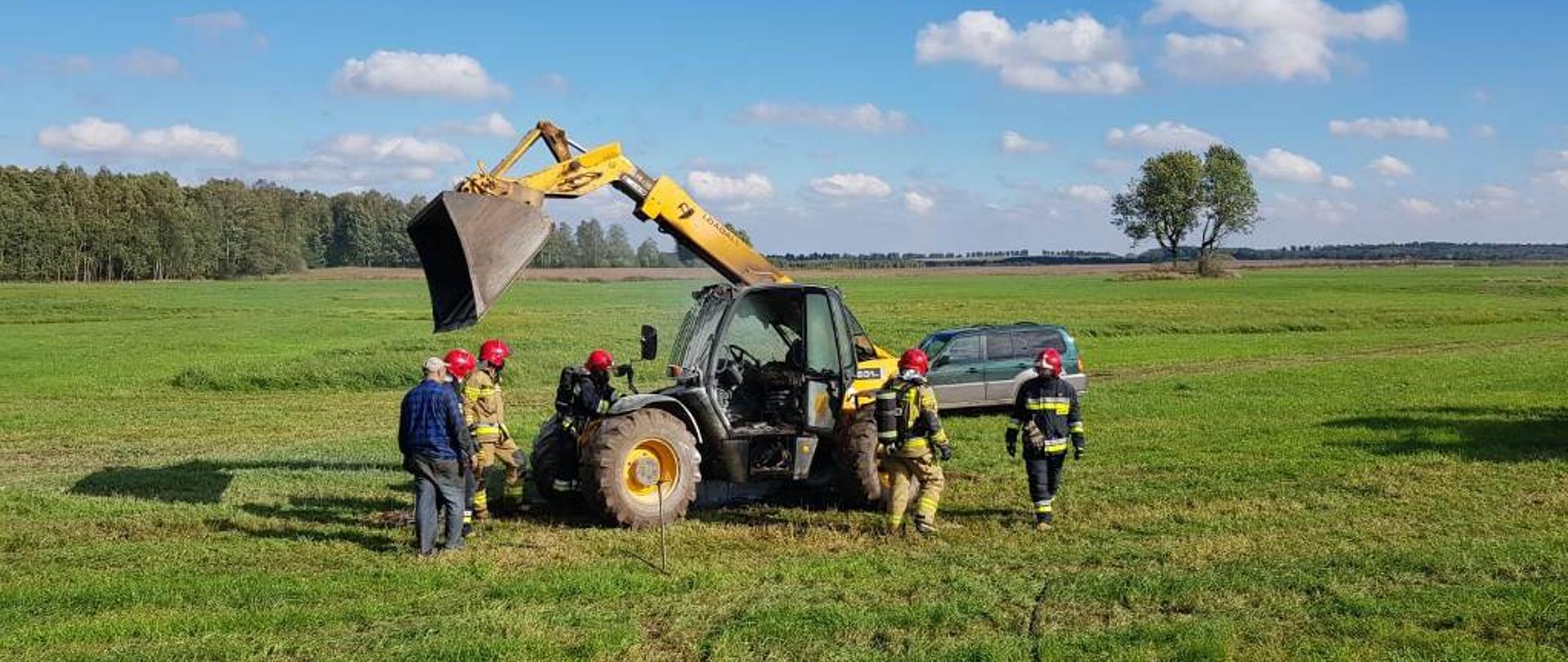 Strażacy podczas akcji gaszenia ładowarki kołowej palącej się na polu