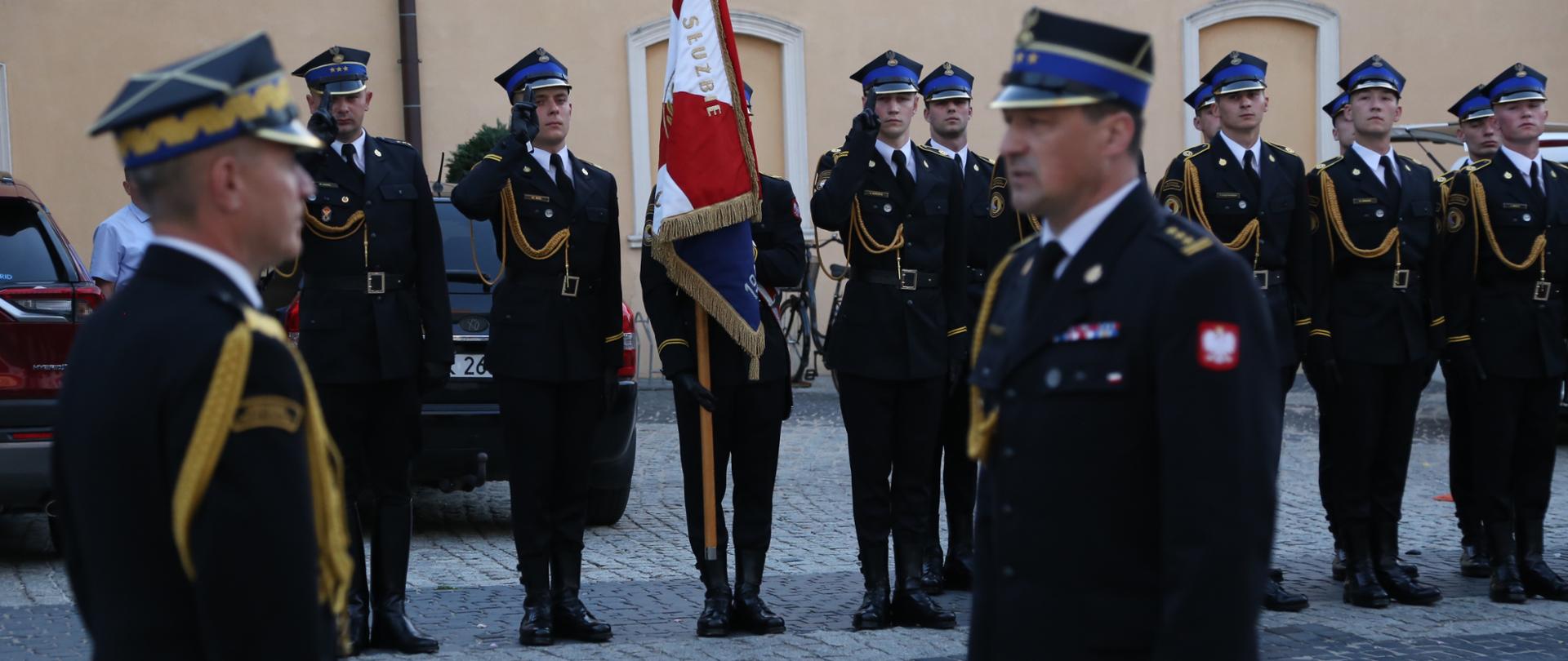 Komendant CS PSP w Częstochowie składa meldunek Komendantowi Głównemu PSP, w tle w dwuszeregu ustawiona kompania reprezentacyjna Centralnej Szkoły PSP wraz z pocztem sztandarowym