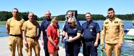 Na zdjęciu przedstawiciele służb uczestniczących w patrolach, stoją na pomoście, w tle jezioro i las.