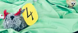 Fragment dekoracji koncertu wiosennego .Na zielonym materiale umieszczone są prace plastyczne dzieci związane z tematyką wiosenną. Przy każdej pracy podany jest numer w postaci żółtej kartki