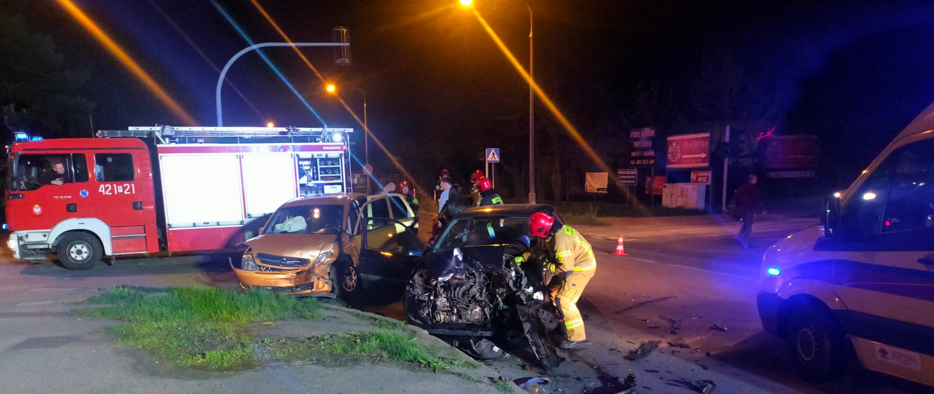 Na zdjęciu widać przody dwóch uszkodzonych samochodów osobowych, które zderzyły się w obrębie skrzyżowania. Jest pora nocna