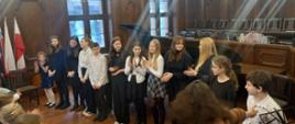 Zdjęcie przedstawia grupę uczniów - wykonawców koncertu w zabytkowej sali.