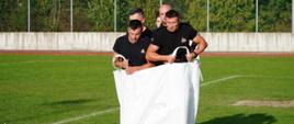 Na zdjęciu widocznych pięć osób w czarnych koszulkach w białym worku big bag na stadionie sportowym biorą udział w jednej z konkurencji w XXXI Spartakiady HDK PCK w Ropie
