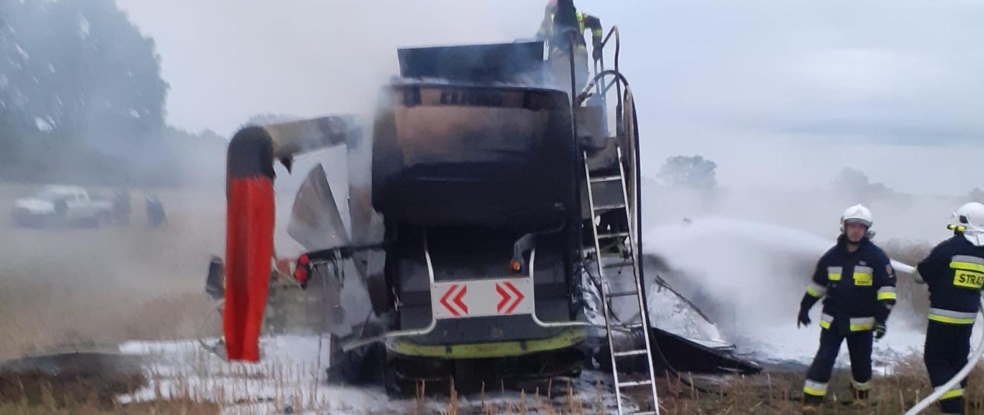 Na zdjęciu spalony kombajn podczas prac polowych. Obok strażacy, którzy go ugasili.