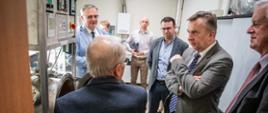 Minister Wieczorek i kilku mężczyzn w garniturach stoją w laboratorium.