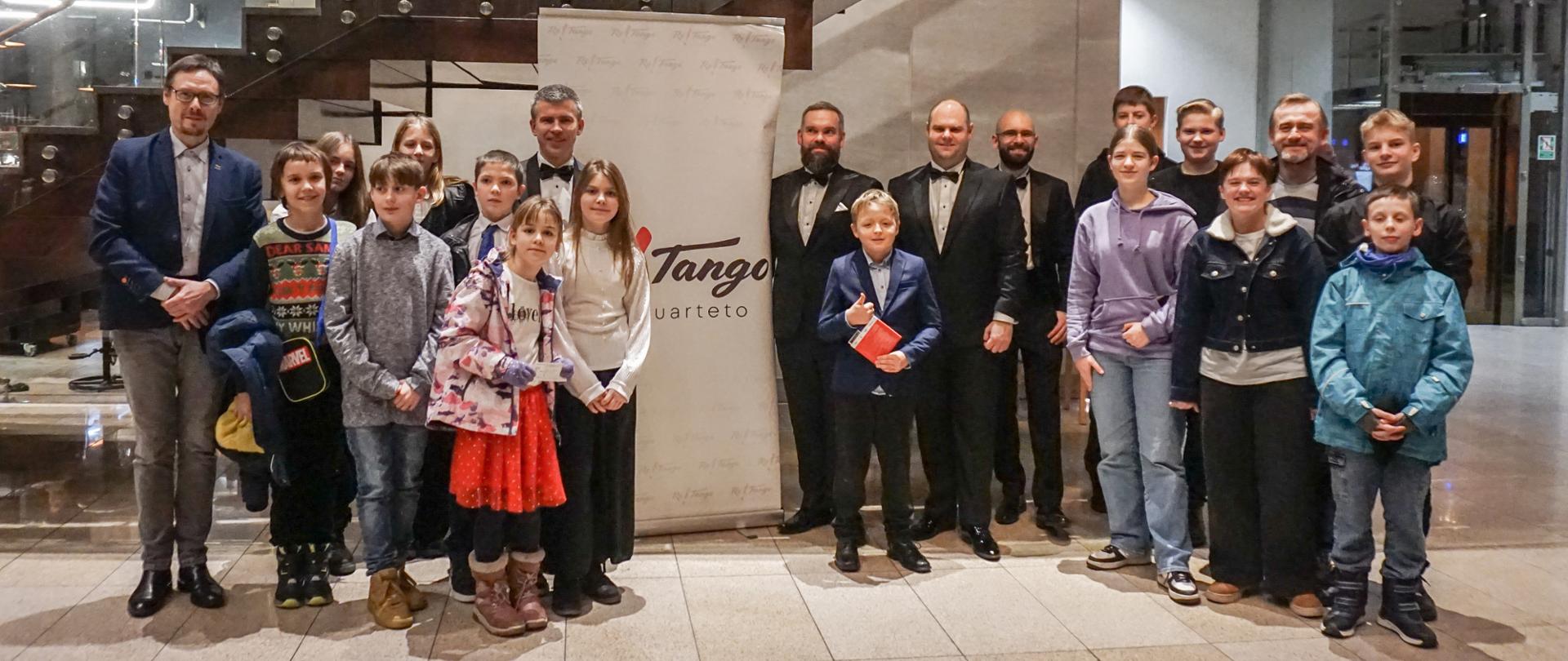 We foyer Filharmonii Kaszubskiej pozują do zdjęcia na stojąco uczniowie klasy akordeonu wraz z artystami zespołu Tango Re Quarteto