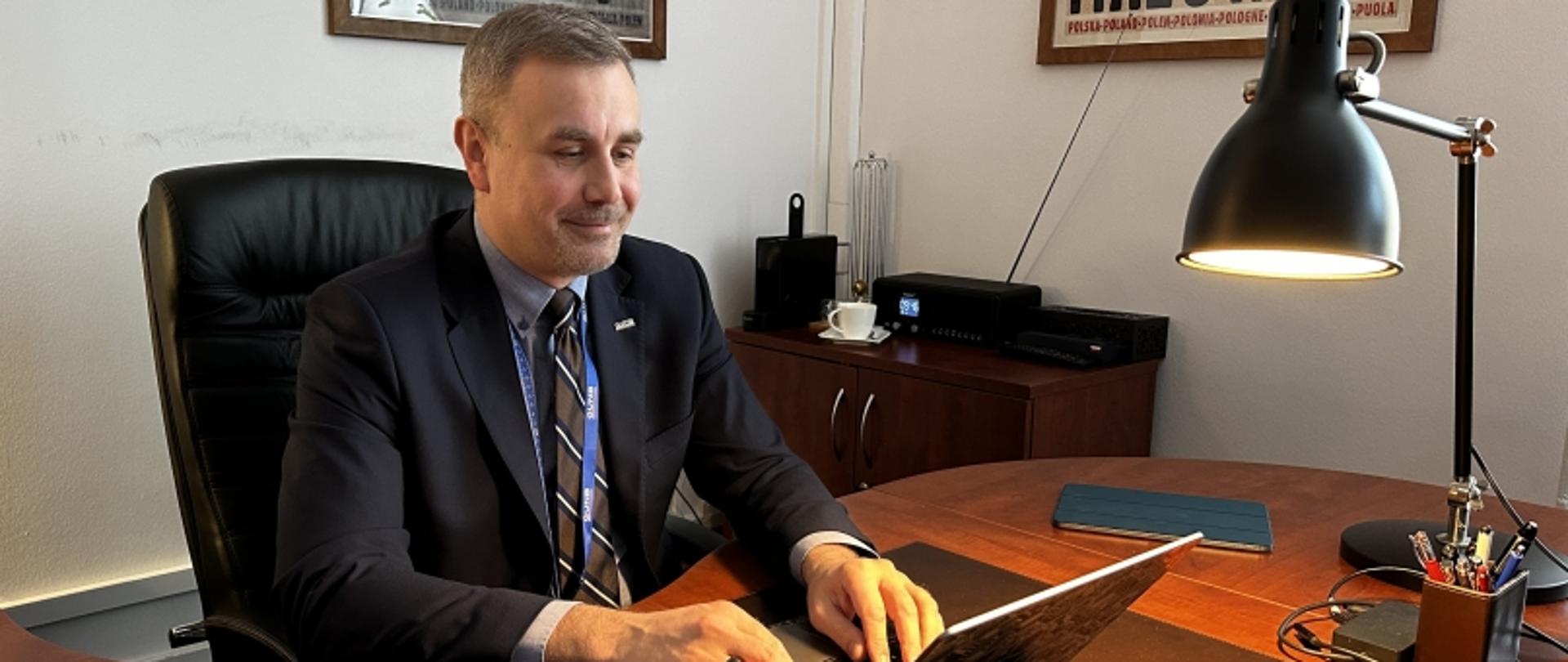 Pracownik przy biurku z laptopem i kubkiem kawy w biurowym otoczeniu.