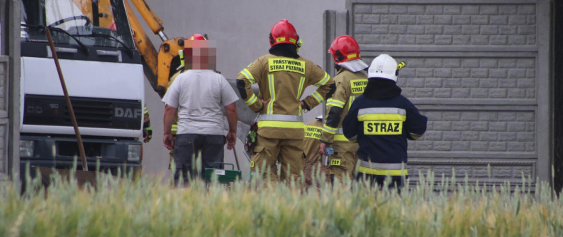 Na zdjęciu znajdują się strażacy podczas usuwania zagrożenia związanego z uszkodzony gazociąg. Na zdjęciu widać także samochód ciężarowy oraz koparkę.