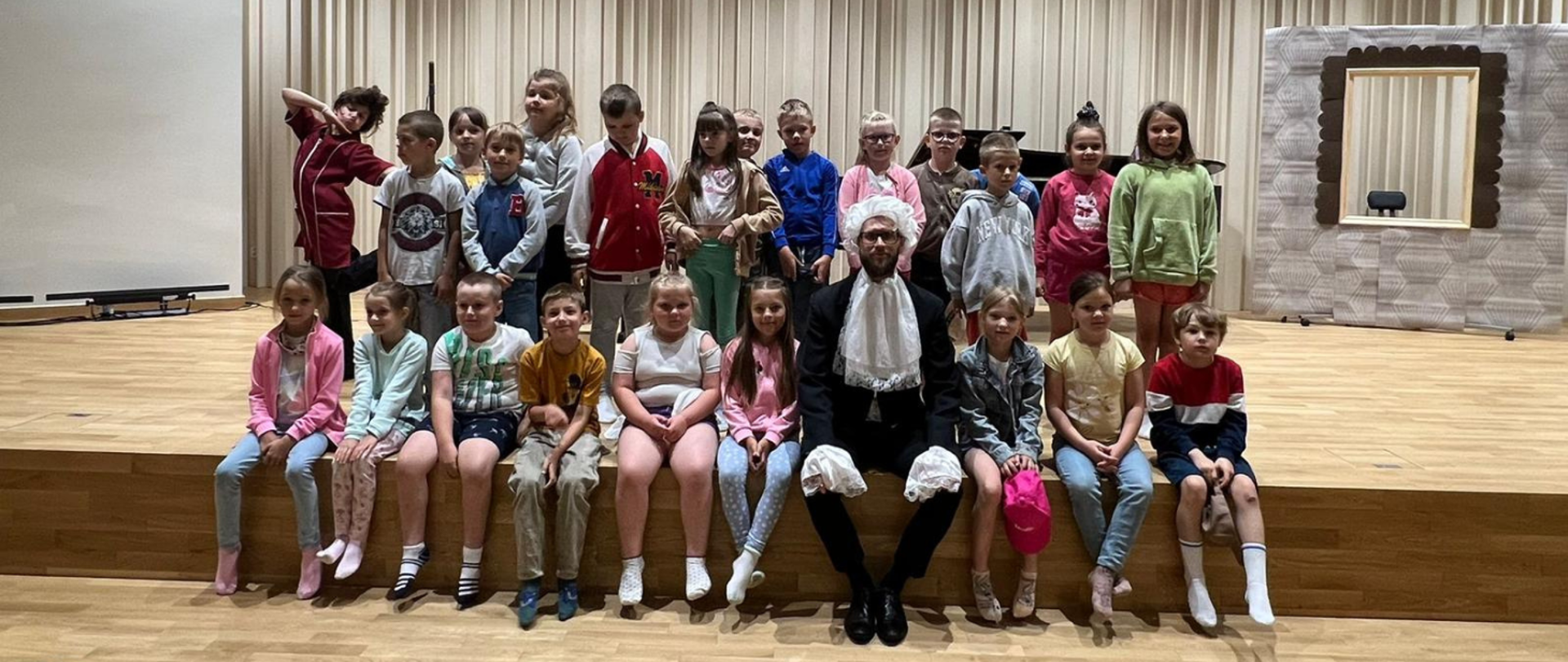 Pamiątkowe zdjęcie grupy uczniów ze szkoły ze Stężycy, którzy uczestniczyli w koncercie rekrutacyjnym zorganizowanym w naszej szkole. Pomiędzy uczniami siedzi mężczyzna w białej peruce i żabocie.