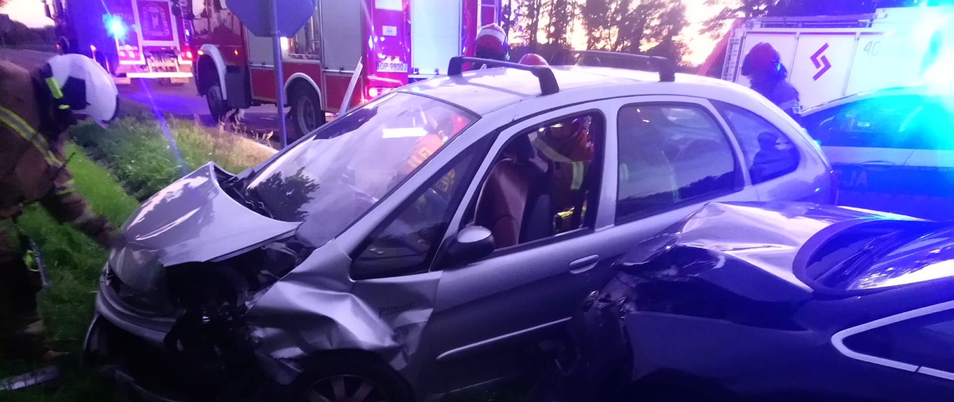 Wypadek samochodowy na drodze powiatowej nr. 1179O w pobliżu Gierszowic - zdjęcie przedstawia 2 samochody osobowe uczestniczące w wypadku. W tle widać pojazd pożarniczy.