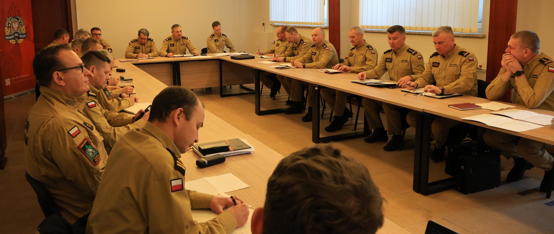 W piątek 9 stycznia br. w świetlicy Komendy Miejskiej Państwowej Straży Pożarnej w Białymstoku odbyła się odprawa z komendantami powiatowymi i miejskimi PSP z terenu województwa podlaskiego - funkcjonariusze w żółtych mundurach siedzą przy stołach podczas odprawy