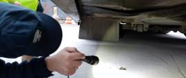 Inspektor ITD podświetla latarką plamę oleju z silnika kontrolowanego autokaru.