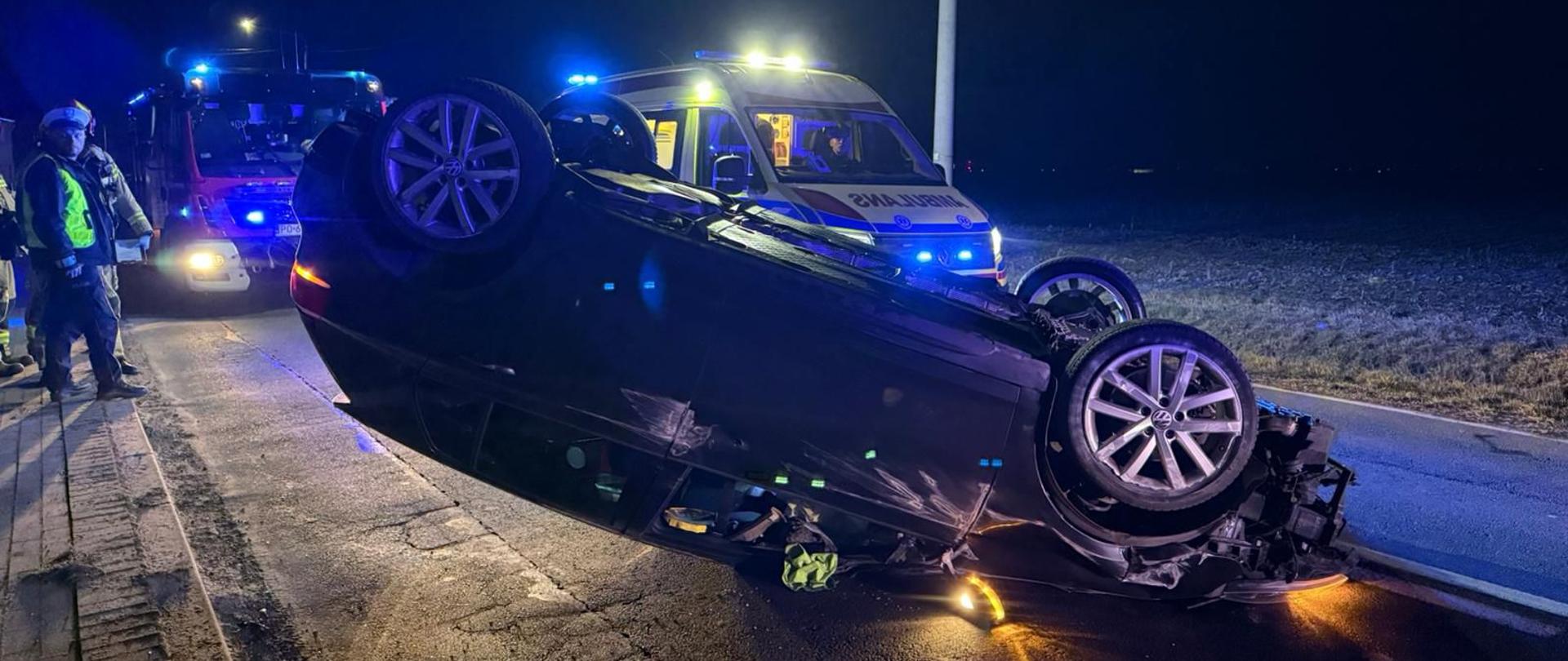 samochód osobowy na dach za nim karetka pogotowia oraz samochód straży pożarnej