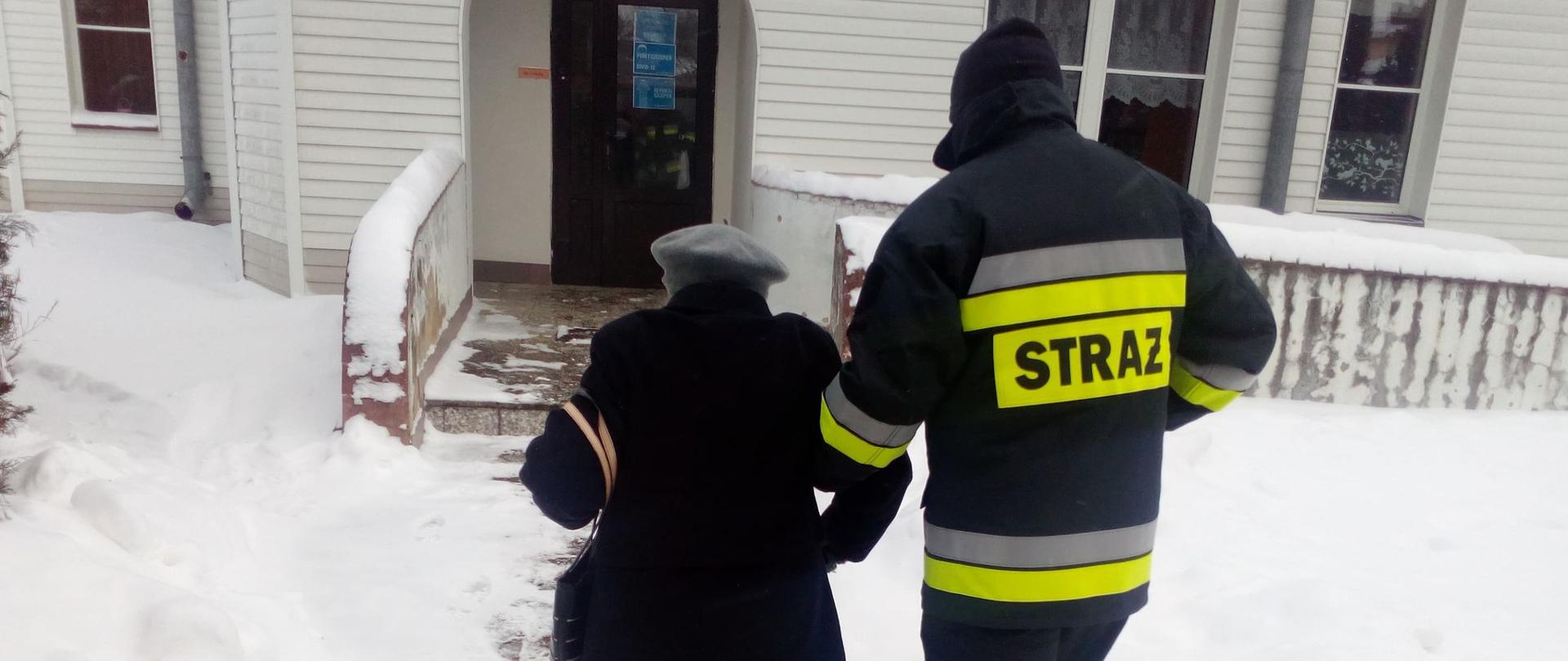 Strażak pomagający kobiecie w podeszłym wieku przejść do punktu szczepień