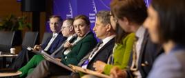 Wiceminister rozwoju i technologii Olga Semeniuk podczas debaty EKG nt. transformacji cyfrowej – regulacji i etyce, pani minister siedzi i przemawia przez mikrofon, obok niej siedzą pozostali uczestnicy panelu, pierwszy po lewej prezes UOKiK Tomasz Chróstny.