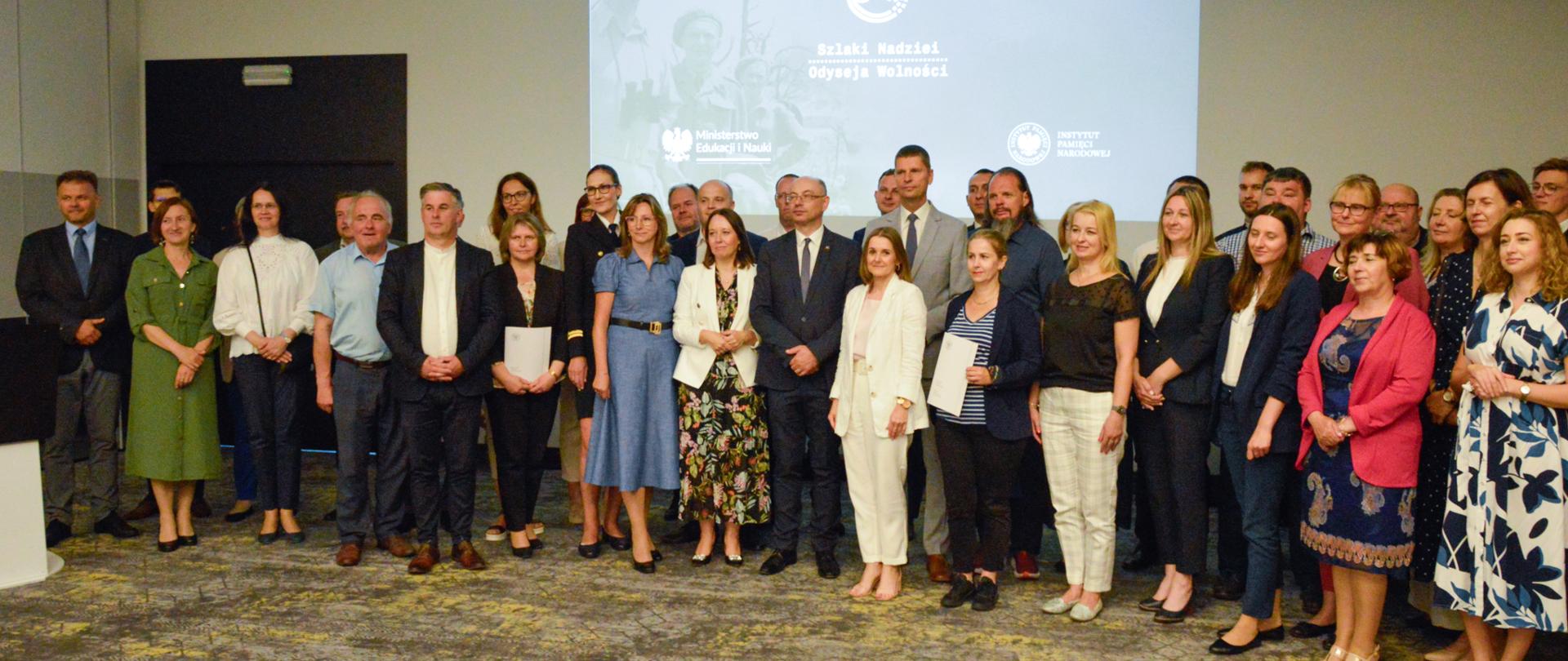 Zdjęcie zbiorowe, na sali pod ścianą stoi duża grupa ludzi.