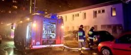 Na zdjęciu widoczny jest budynek w którym miał miejsce pożar, pracujący strażacy oraz samochód straży