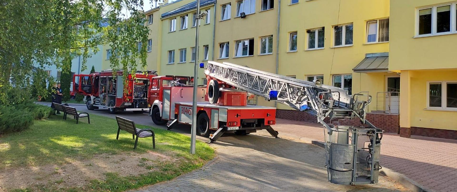 Zdjęcie przedstawia dwa samochody pożarnicze w tym drabinę mechaniczną stojące na podjeździe przy budynku Domu Opieki Społecznej.