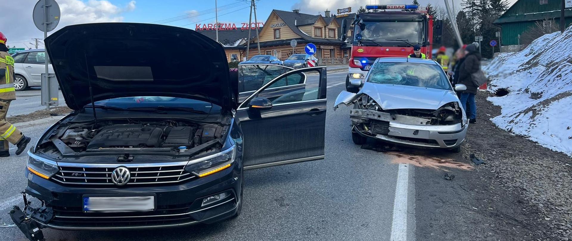 Dwa rozbite samochody osobowe. Jeden z nich ma otwartą klapę silnika.