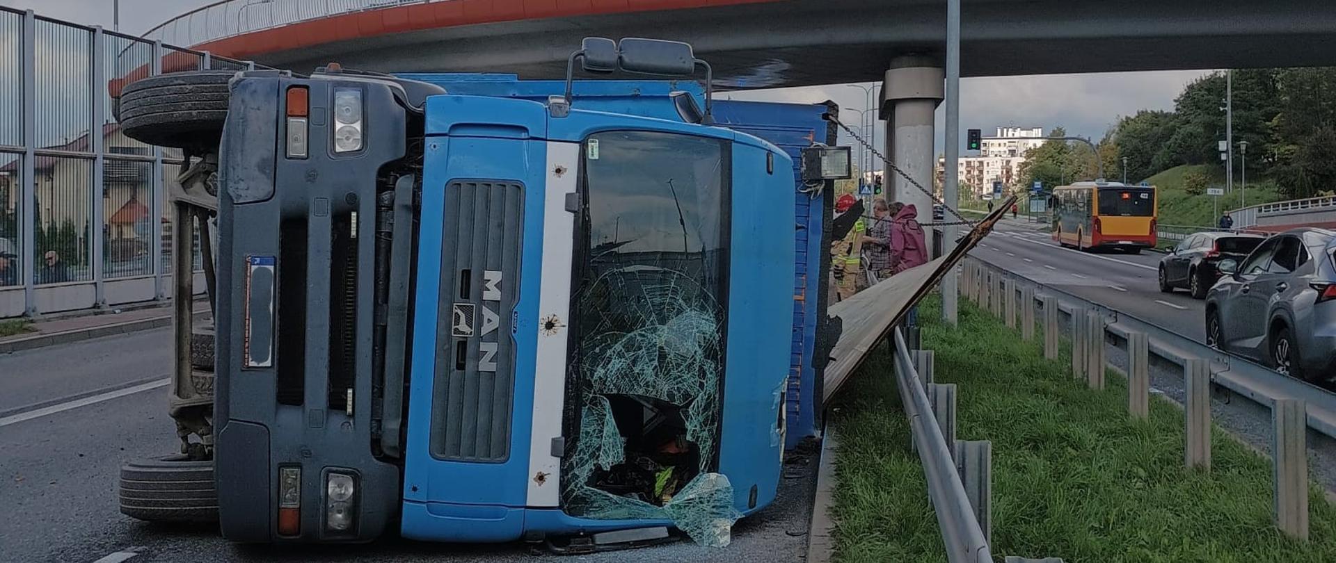 Zdjęcie przedstawia ulicę Grunwaldzką w Kielcach. W centralnym punkcie leży na boku ciężarówka przewożący kontener budowlany.