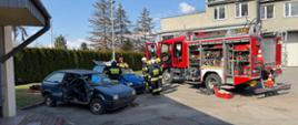 druhowie w trakcie egzaminu epizodu z zakresu ratownictwa technicznego widoczne wraki pojazdów osobowych w tle samochód pożarniczy