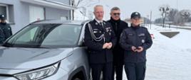 Mężczyzna w galowym mundurze, wojewoda stoi z kobietą w mundurze roboczym oraz mężczyzna w czarnym płaszczu. Stoją przy nowym samochodzie 