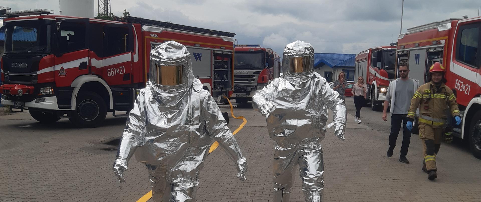 Strażacy w ubraniach żaroodpornych udają się w strefę działań gaśniczych, w trakcie ćwiczeń