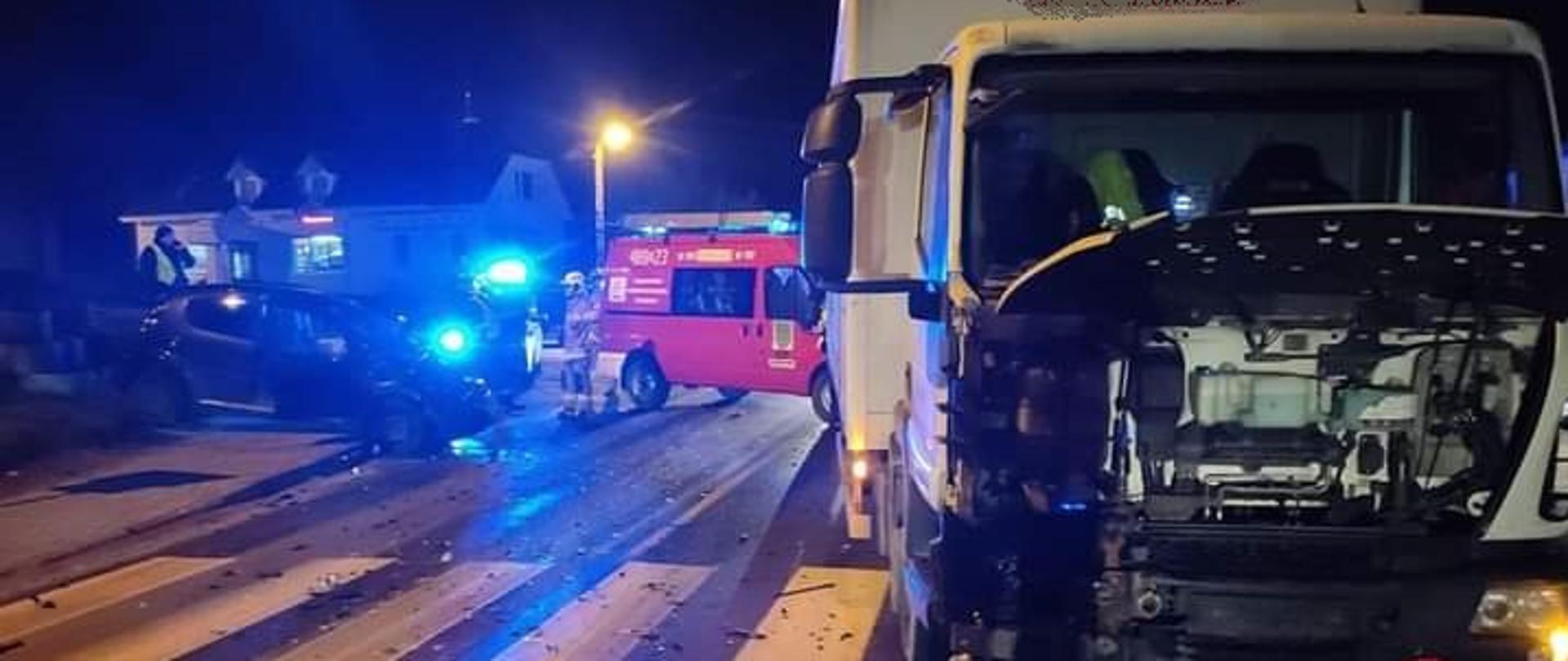 Po lewej stronie rozbity samochód osobowy. Po prawej stronie samochód dostawczy biorący udział w zdarzeniu. Pomiędzy nimi samochód strażacki. Przód samochodu dostawczego stoi na przejściu dla pieszych.