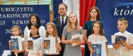 Sześcioro młodzieży stoi w szeregu, trzymają w rekach książki, za nimi wiceminister Bernacki i dwie kobiety.
