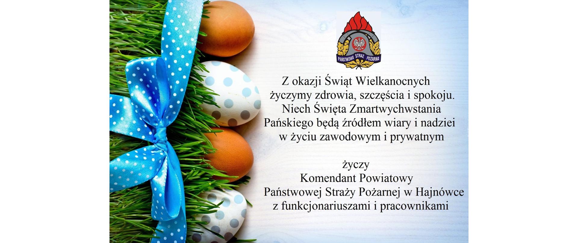 Po lewej stronie na zielonej trawie leżą jajka przewiązane niebieską wstążką. Po prawej stronie pod logiem PSP życzenia Wielkanocne 