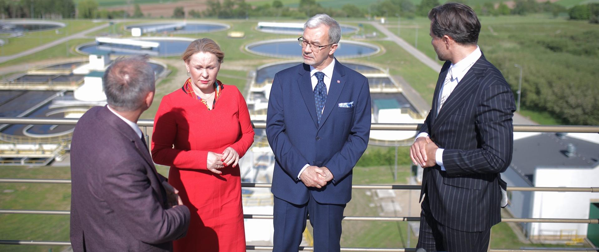 w stronę Jerzego Kwiecińskiego i Andżeliki Możdżanowskiej patrzy dwóch mężczyzn, za nimi w tle oczyszczalnia ścieków