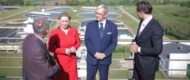 w stronę Jerzego Kwiecińskiego i Andżeliki Możdżanowskiej patrzy dwóch mężczyzn, za nimi w tle oczyszczalnia ścieków