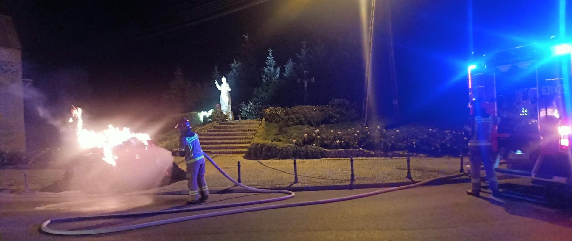 Na zdjęciu widać strażaka gaszącego palący sie balot słomy 