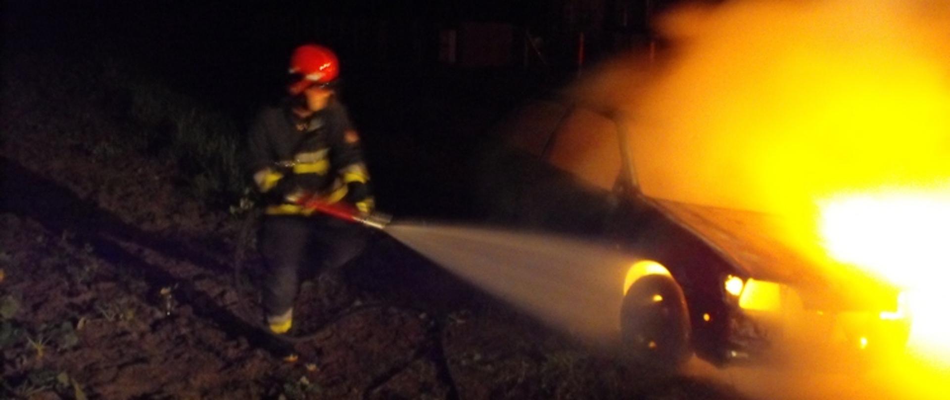 Zdjęcie przedstawia strażaka gaszącego płonący samochód osobowy