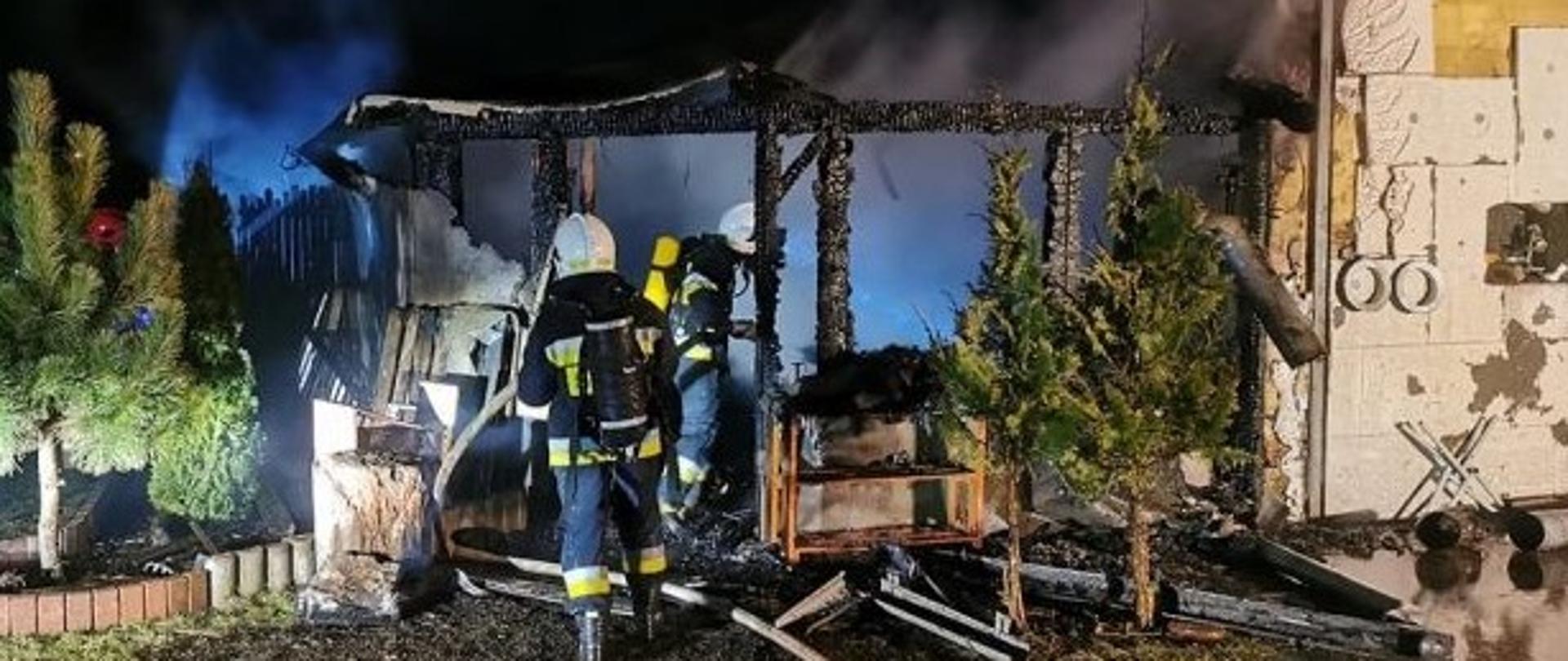 Spalona konstrukcja budynku, dwóch strażaków gaszących ogień, 