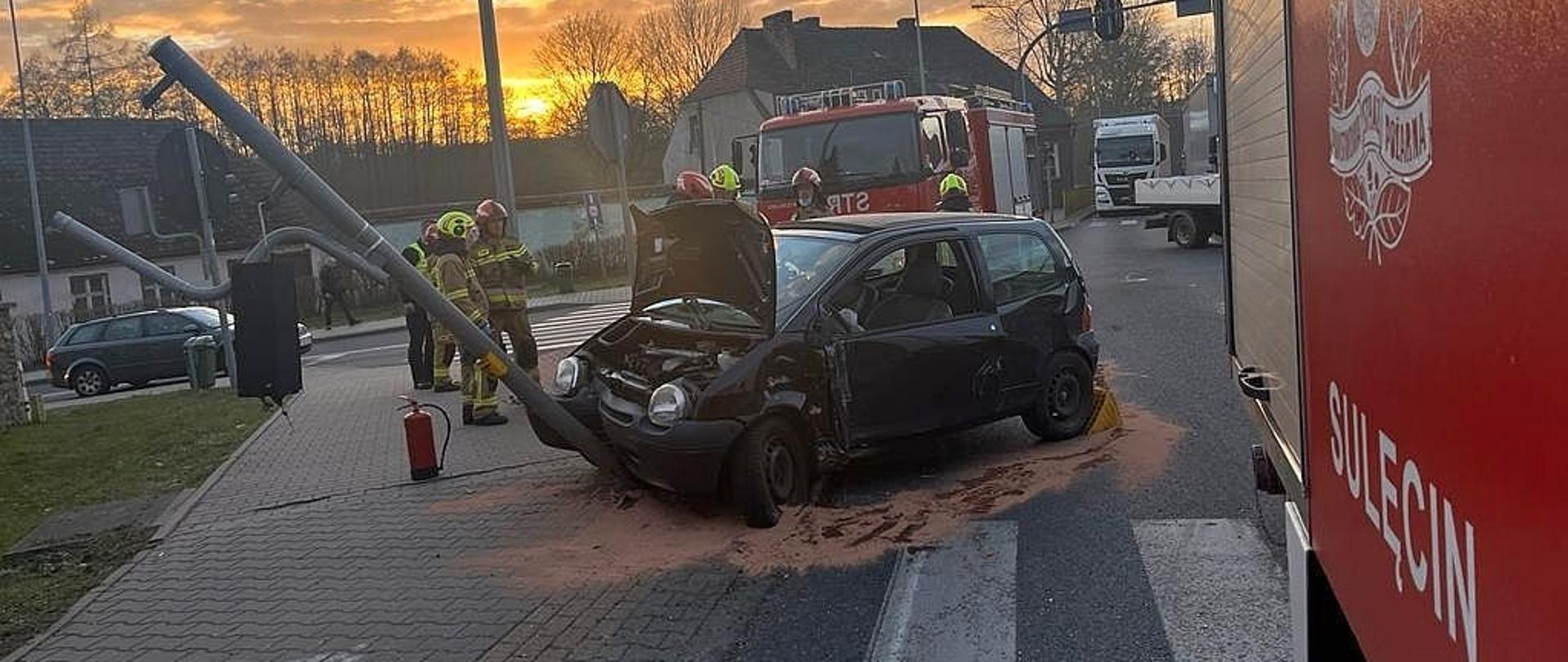 Na zdjęciu znajduje się rozbity samochód oraz samochody pożarnicze