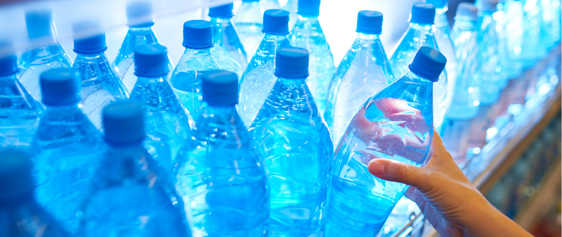 butelki z wodą na sklepowej półce i sięgająca po nie ręka z prawej strony 