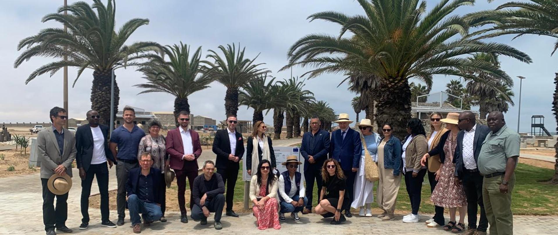 Grupa 21 osób, w tle park i plac zabaw, szpaler palm