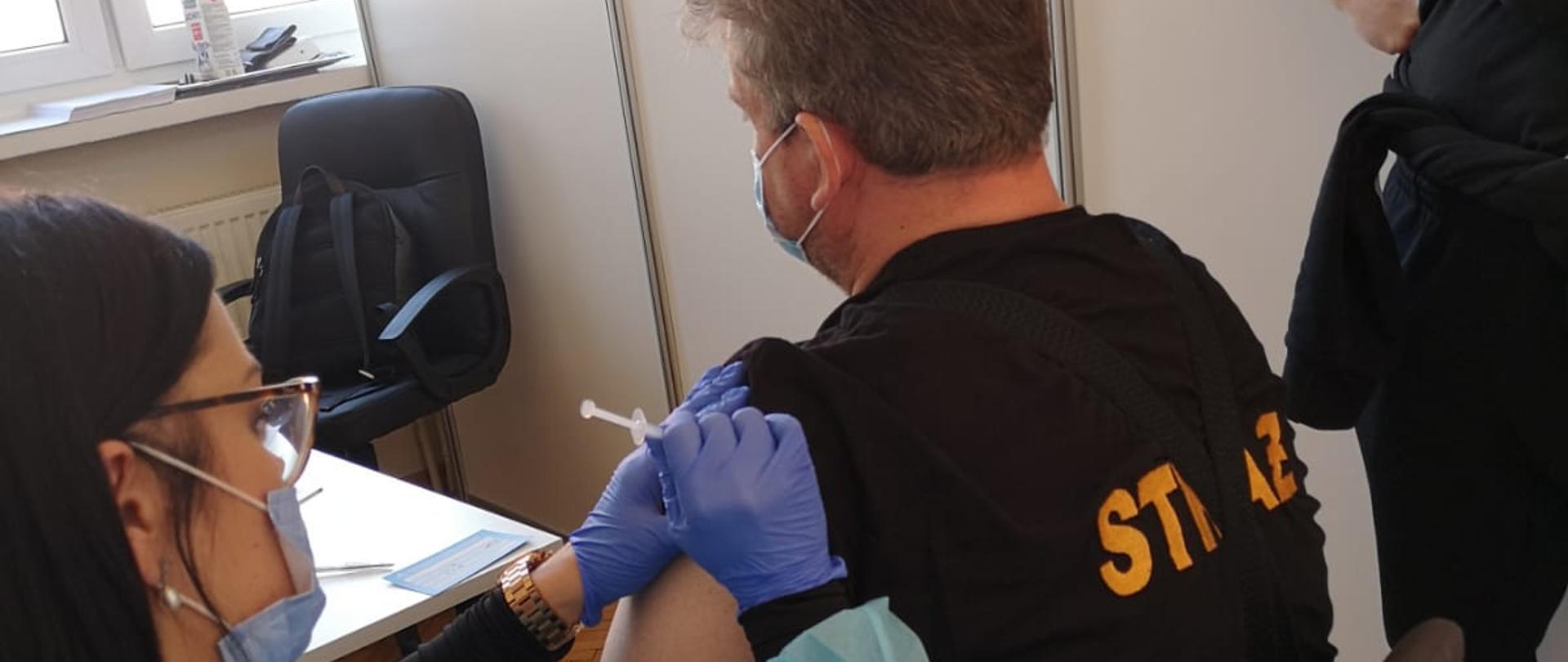 Zdjęcie przedstawia moment zaszepienia przez pielęgniarkę przeciwko Covid-19 druha OSP Templewo w gabinecie lekarskim. 