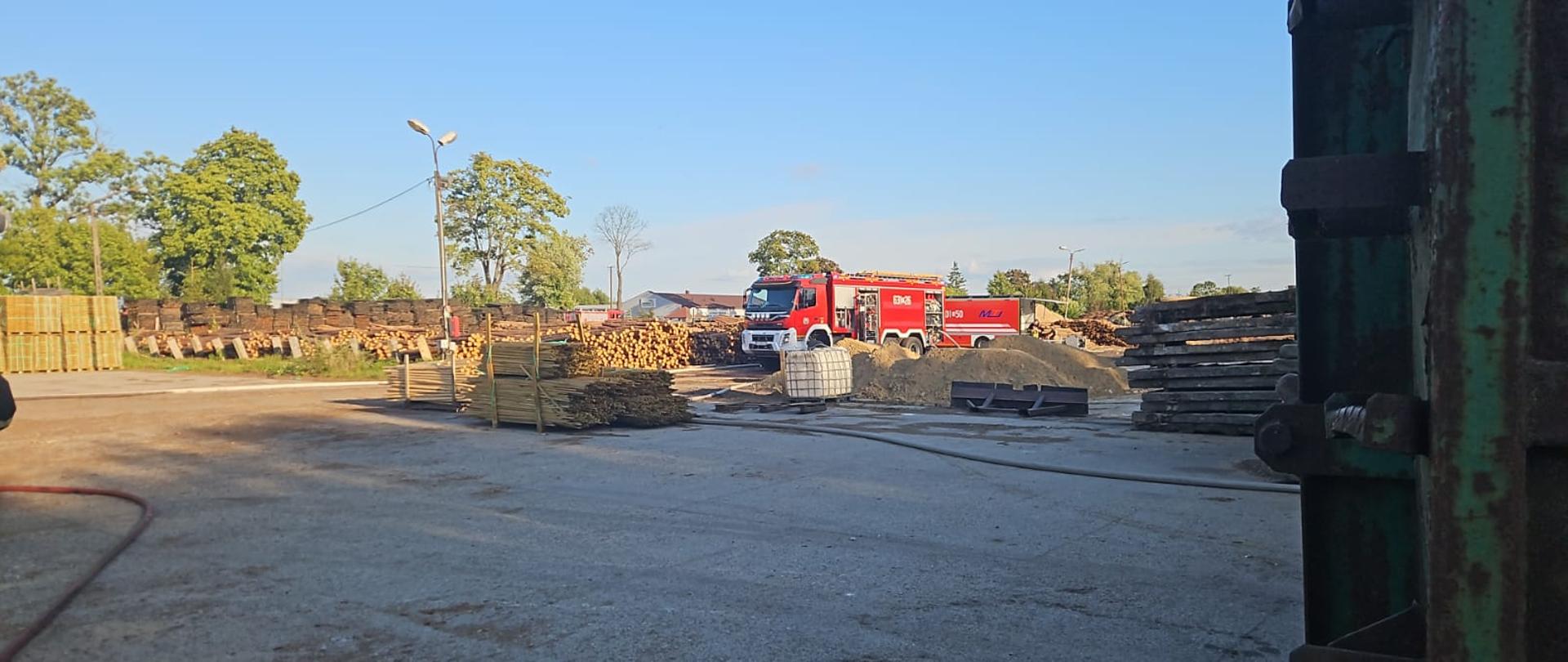 pojazdy gaśnicze na placu zakładu pomiędzy składowanym drewnem