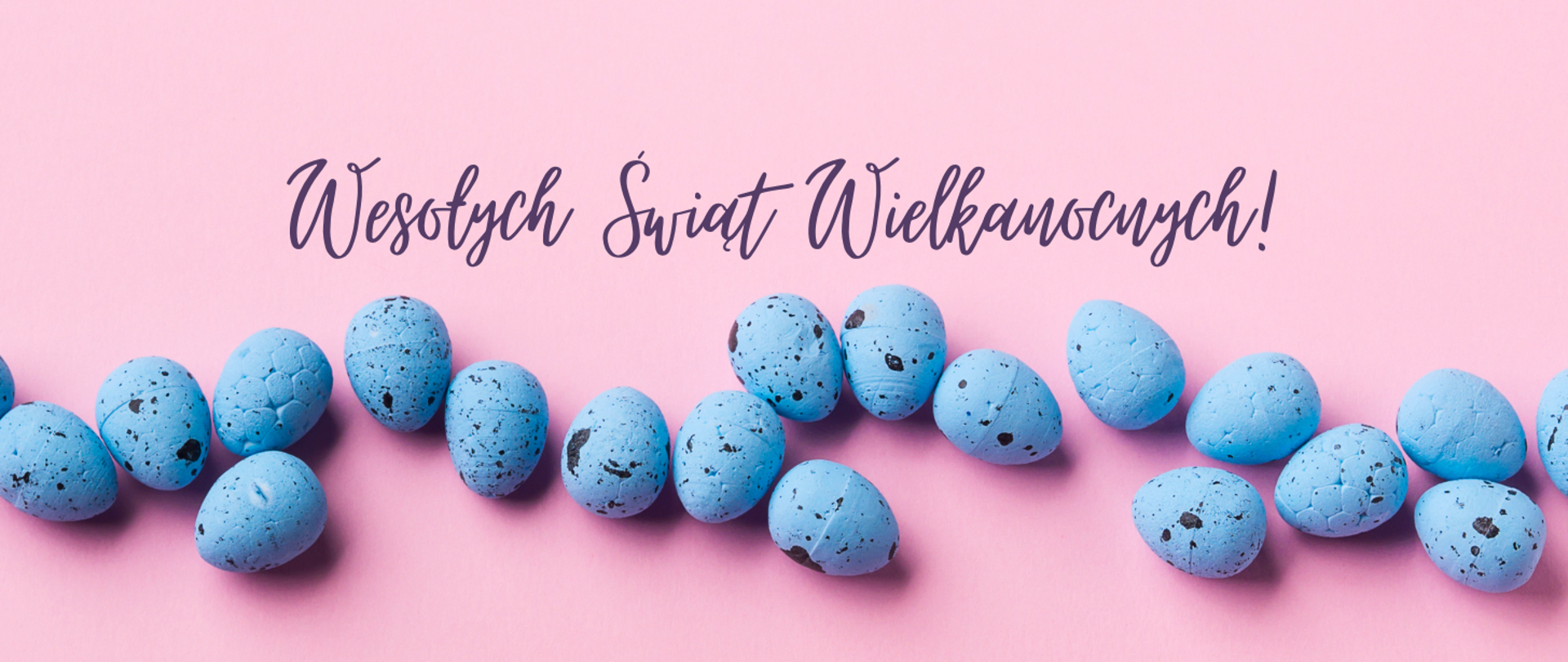 Jasnoróżowy baner z napisem "Wesołych Świąt Wielkanocnych!" napisanym ciemnofioletową, ozdobną czcionką u góry. Poniżej, na środku, znajduje się rząd niebieskich jajek wielkanocnych z małymi, ciemnymi plamkami. Jajka są ułożone blisko siebie, tworząc dekoracyjną linię wzdłuż dolnej części banera.