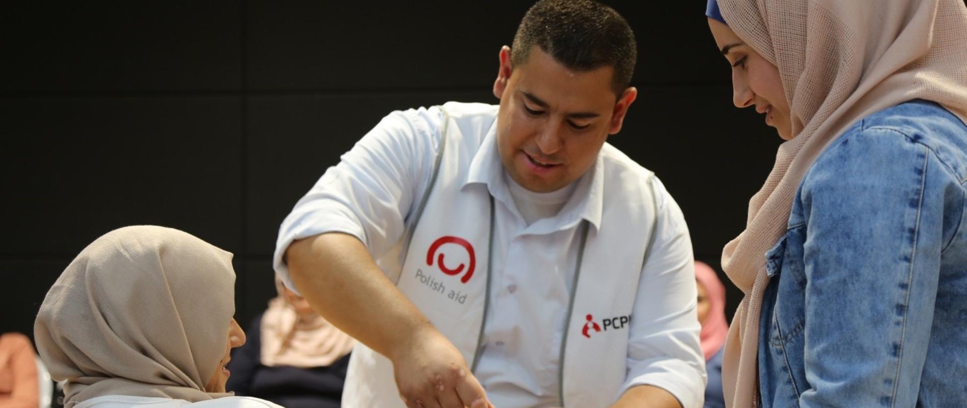 mężczyzna w kamizelce z logo Polskiej pomocy opatruje kobietę