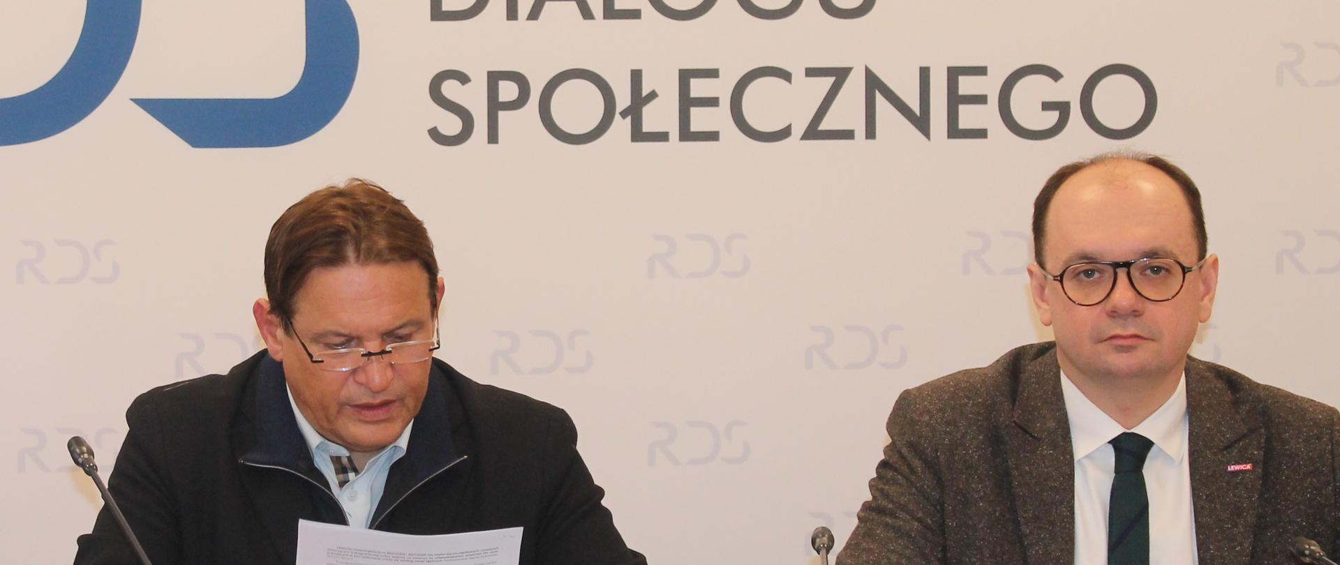 Na zdjęciu widnieje stół prezydialny za którym siedzą: Pan Sebastian Gajewski, Podsekretarz Stanu w Ministerstwie Rodziny, Pracy i Polityki Społecznej oraz Pan Jacek Męcina, Przewodniczący Zespołu ds. prawa pracy. W tle widnieje baner z napisem Rada Dialogu Społecznego