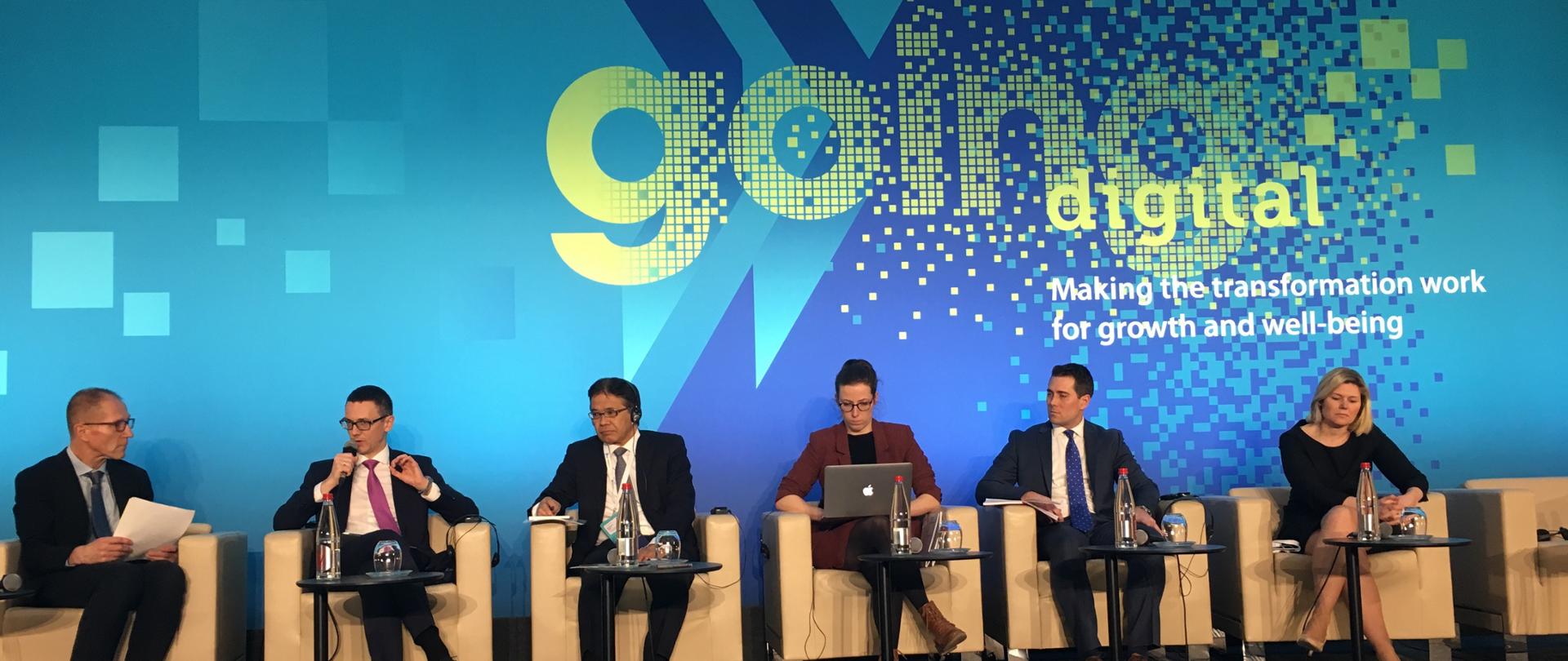 Minister Karol Okoński w panelu dyskusyjnym. Siedzi 6 uczestników. Karol Okoński drugi z lewej. Napis "Going Digital".
