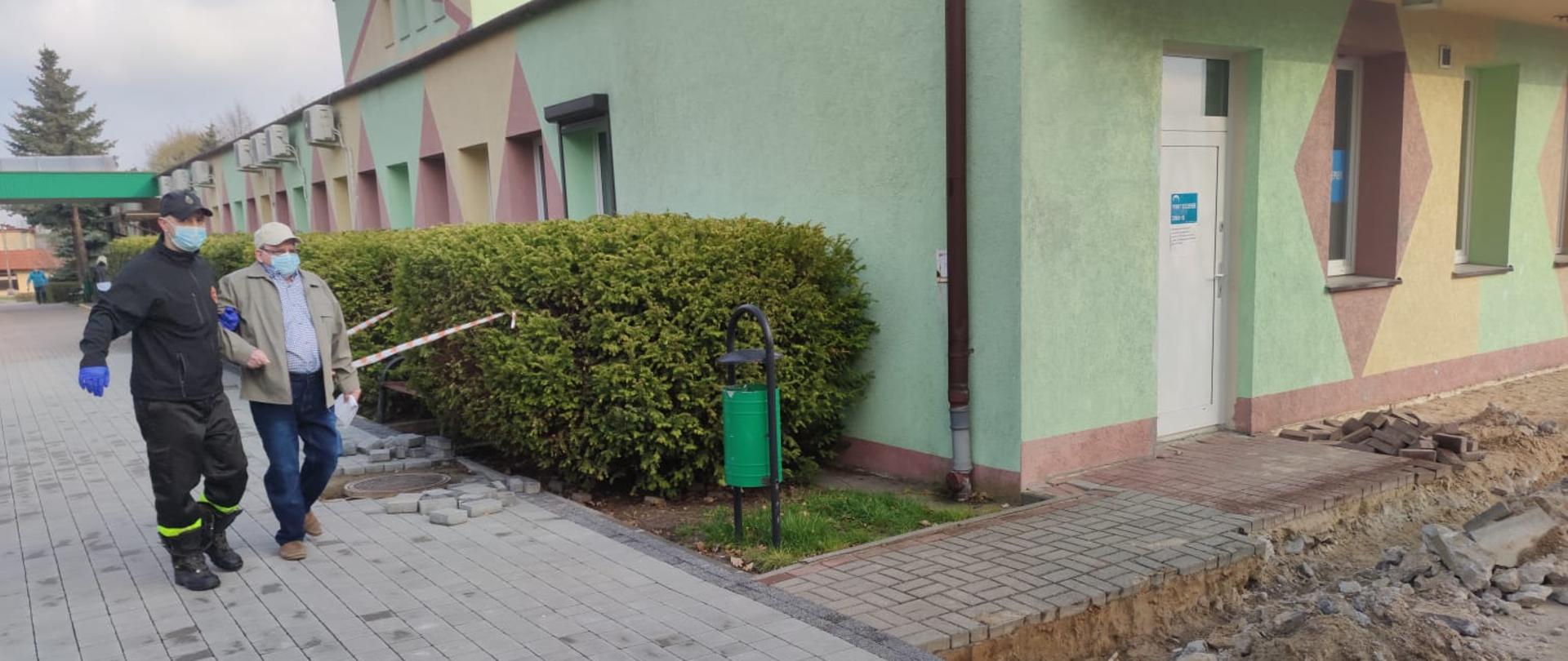 zdjęcie przedstawia funkcjonariusza OSP Barcin prowadzącego starszego Pan do punktu szczepień 