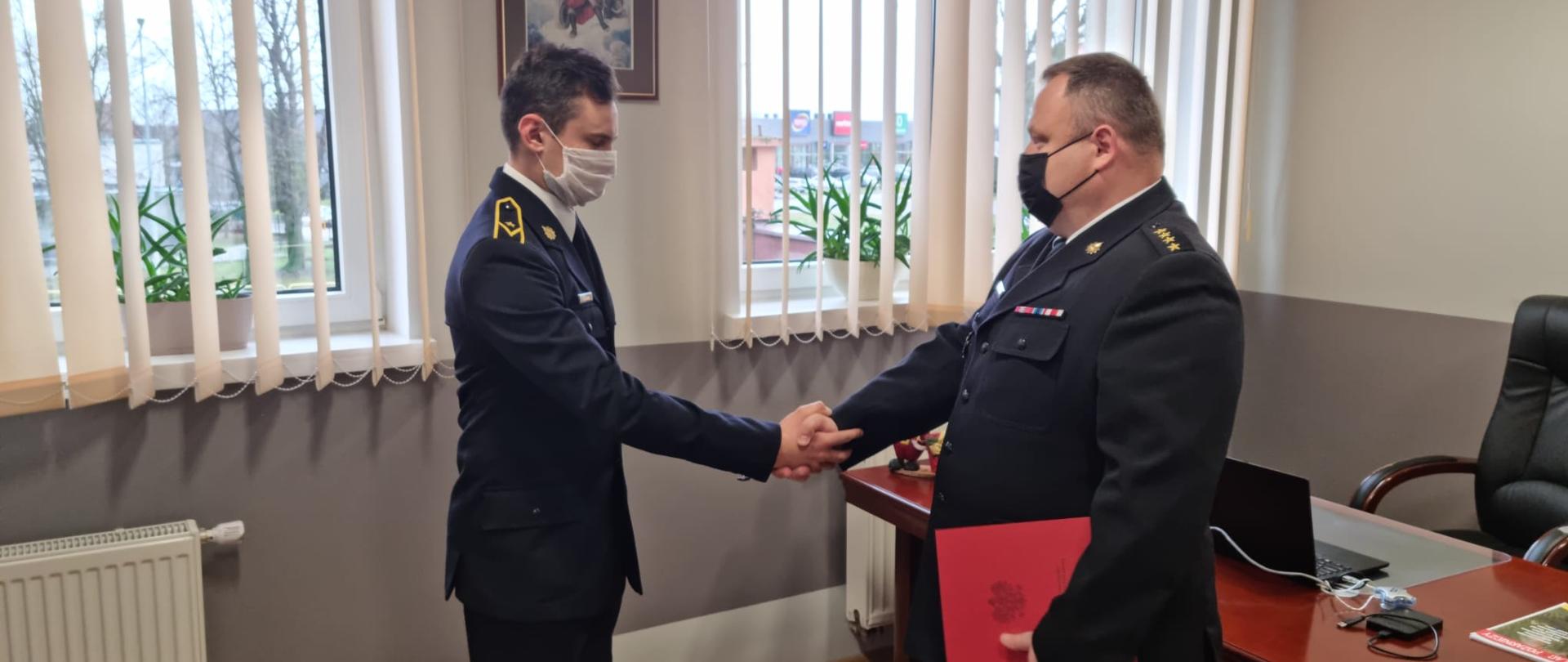 Fotografia przedstawia Komendanta Powiatowego PSP w Malborku w trakcie wręczania nominacji. Funkcjonariusze ubrani są w mundury wyjściowe koloru granatowego. 